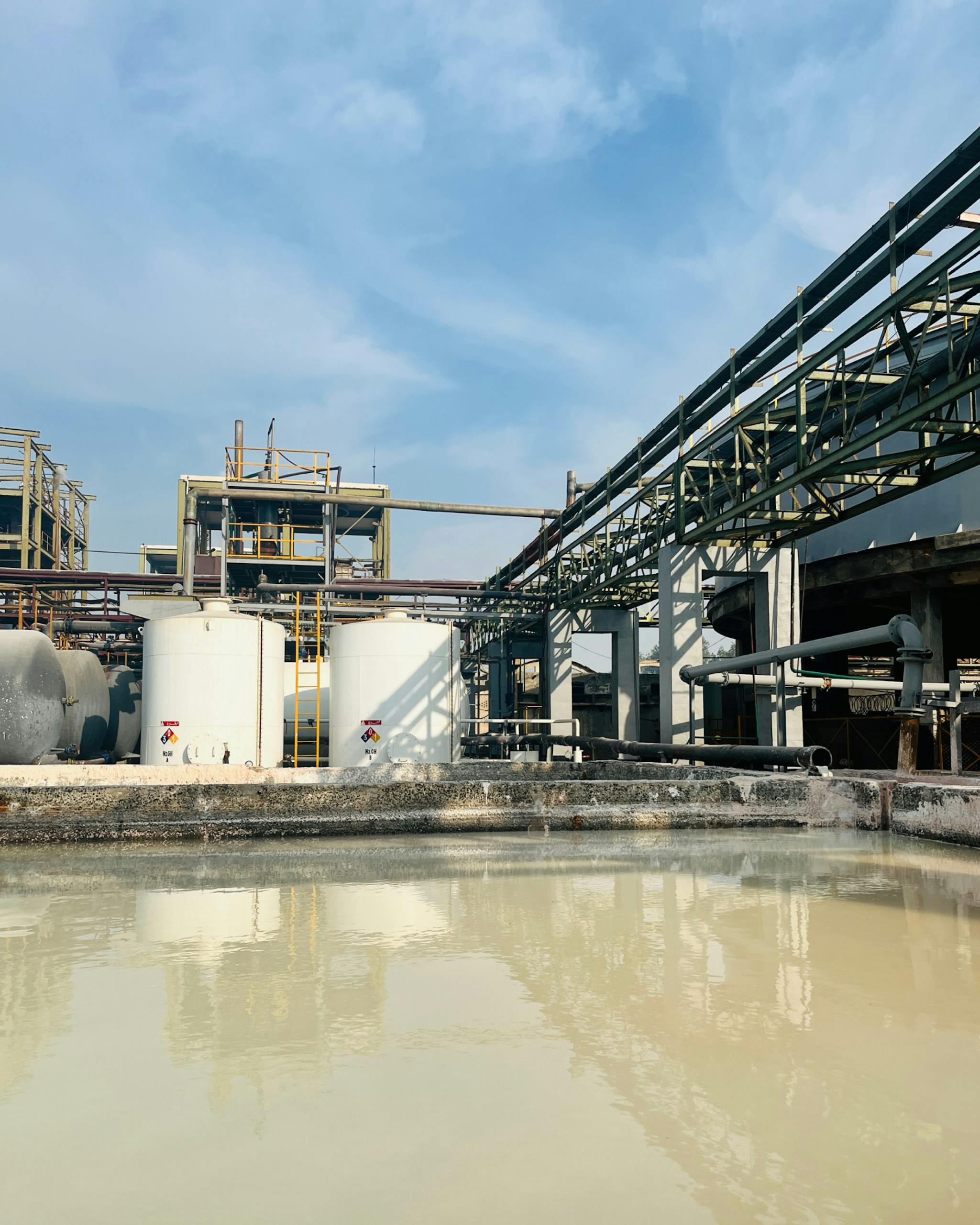 Aerial view of an industrial facility with large water tanks in Faisalabad, Pakistan under a clear sky.