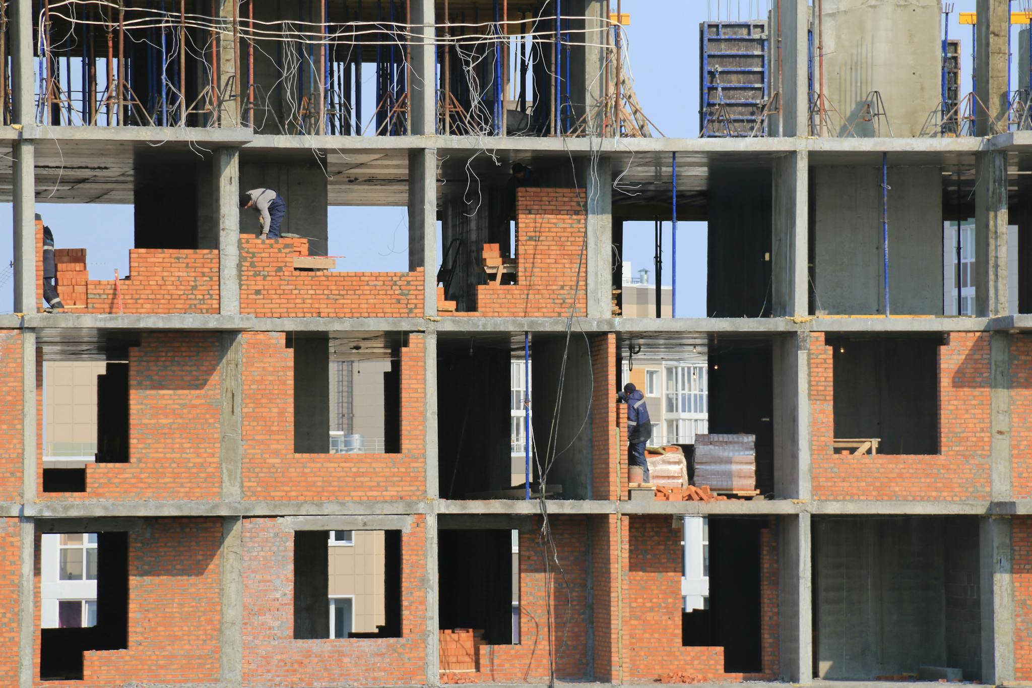 Workers engaged in bricklaying on a multi-story building under construction in an urban area.
